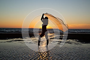 Silhoutte of a pretty senior Asian female in a swimming suit standing and flaunt yellow fabric on the beach.