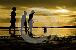 Silhoutte three boys walking toward the ball on water. sunset sunrise and reflection on water