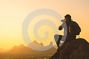 Silhuette of photographer traveler taking photo of beautiful sunset from top of the mountain