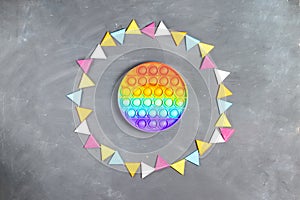 Silicone antistress pop it or simple dimple in a round frame made of colorful felt garland on a gray background