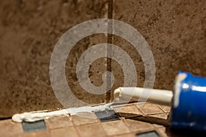 Silicone caulk being applied along a tile joint in a bathroom shower.