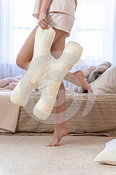 Silk beige beauty pillow against the background of slender sexy female legs close-up. Vertical photo