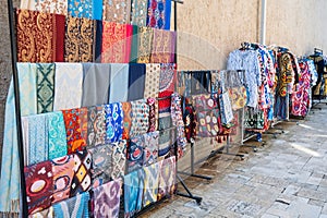 silk scarves, fabric bags and dresses with a traditional bright colorful Asian pattern at oriental bazaar in Uzbekistan