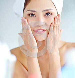 Silky smooth skin. An attactive young Asian woman applying moisturizer with a towel on her head.