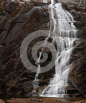 Silky waterfall flowing over vertical rock formation, long exposure, space for text