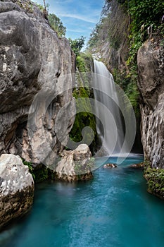 Silky waterfall between rock walls and vegetation with turquoise pond called `Fuentes del Algar` in Callosa de ensarria, Alicante,