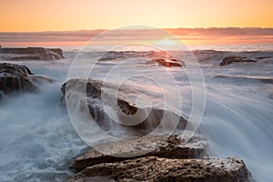 Silky waves splash over sharp rocks at sunrise