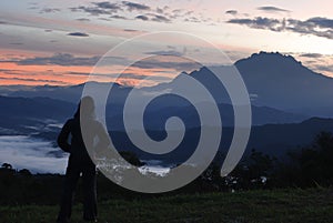 Sillhouette of a woman enjoying the early dawn with Mount Kinabalu as background