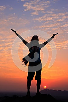 Sillouetted woman with her arms up at sunset on top of the hill, Pushkar, India