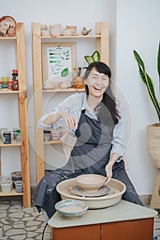 Silly brunette laughs distracting from work on a pottery wheel