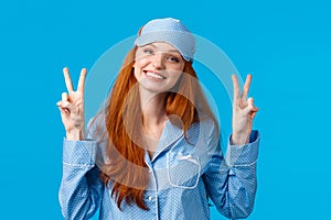 Silly and cute young redhead caucasian girl in sleep mask and nightwear, wearing lovely pyjama feeling alright, showing