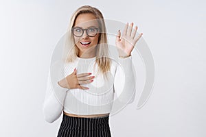 Silly and flirty blond female in elegant white sweater skirt, raising arm and holding palm on heart to pledge and swear