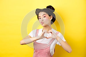 Silly japanese girl showing heart gesture and wishing happy Valentines day, pucker lips to kiss lover, standing on