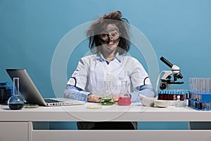Silly looking crazy chemist with messy hair and dirty face sitting at desk after failed laboratory experiment explosion.