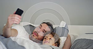 Silly, selfie and father with child in a bed happy, bond and embrace in their home. Goofy, face and kid with parent in a