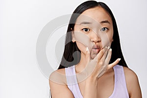 Silly young asian woman poking and sqeezing her face, pucker lips cute, making funny adorable facial expression, white