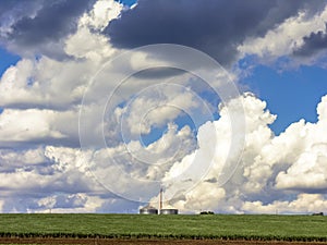 Silo and green corn field with many clouds in sky