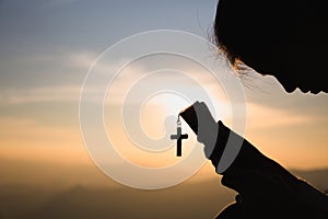 Siluette of Christian woman  holding a bible and wooden Christian cross necklace while praying to God