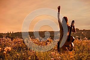 siluette of woman wearing a bohemian style holding a guitar on a field at sunset photo