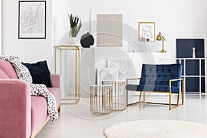 Silver painting on the wall of trendy living room with two elegant coffee tables, petrol blue armchair and powder pink photo