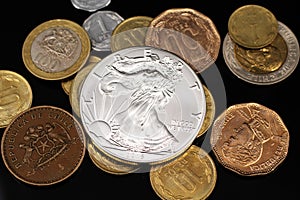 A silver American coin with coins from Pakistan on a black reflective background