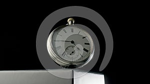 Silver antique pocket watch on a stand rotating on a black isolated background. Round gray retro clock with a white dial
