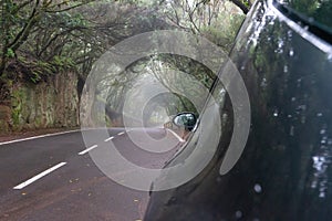 Silver auto in creepy forest and foggy route in a journey to scape, driving with safety in an asphalt mountain road. Car parked