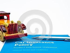 A silver ball pen and one wooden vintage toy car over blue insurance papers shot against white background