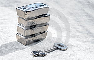 Silver bars and the key to the safe against a rough texture of the fabric