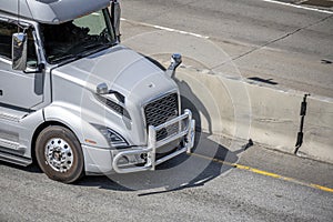 Silver big rig semi truck tractor with grille guard driving on the highway road