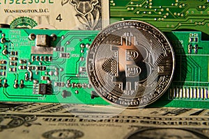 Silver bitcoin coin with dollars and computer motherboard, cryptocurrency mining and investing