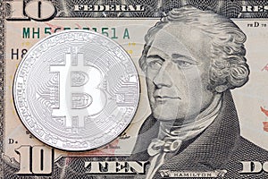 Silver bitcoin coin on ten dollars banknote close up.
