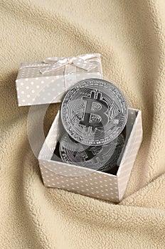 The silver bitcoin lies in a small orange gift box with a small bow on a blanket made of soft and fluffy light orange fleece