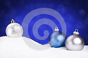 Silver and blue Christmas baubles on snow, blue background