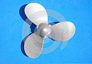 Silver boat propeller on light blue background. Small propeller used for hobby boat and yacht engines. Nautical-inspired