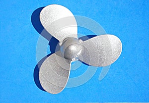 Silver boat propeller on light blue background. Small propeller used for hobby boat and yacht engines. Nautical-inspired photo