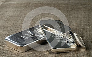 Silver bullion. Cast and minted silver bars and coins against the background of the texture of coarse cloth.