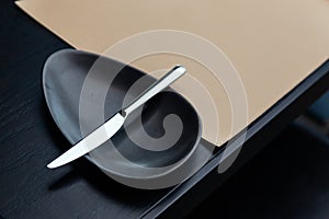 Silver butter knife on black bowl on the wooden table with leather mat. For Fine Dining and European food with copy space