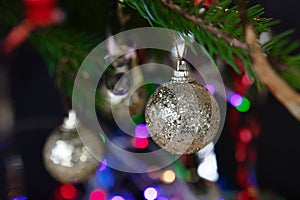 Silver Christmas balls on a branch, lights of garlands in the background