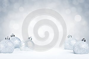 Silver Christmas baubles on snow with a silver background