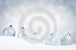 Silver Christmas baubles on snow with a silver background