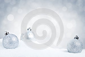 Silver Christmas baubles on snow with a silver background