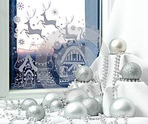 Silver christmas decorations and beads with pedestals on windowsill at night, festive window at New Year holiday or Xmas