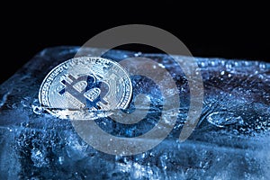 The silver coin of cryptocurrency Bitcoin is freezing in ice