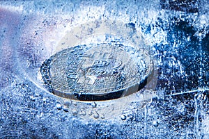 The silver coin of cryptocurrency Bitcoin is freezing in ice