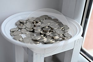 Silver coins on a white saucer. The accumulation of coins. Picking up money for vacation