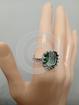 Silver color bijou ring with green stone on mannequin hand