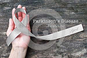 Silver color ribbon on hand support isolated with clipping path for Parkinson`s disease awareness and Brain cancer tumor illness photo