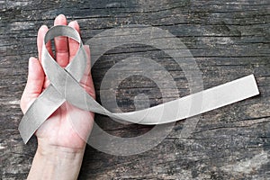 Silver color ribbon on hand support and ols aged wood isolated with clipping path for Parkinson`s disease awareness and Brain
