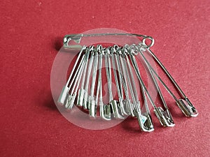 Silver colored safety pins of various sizes on red paper